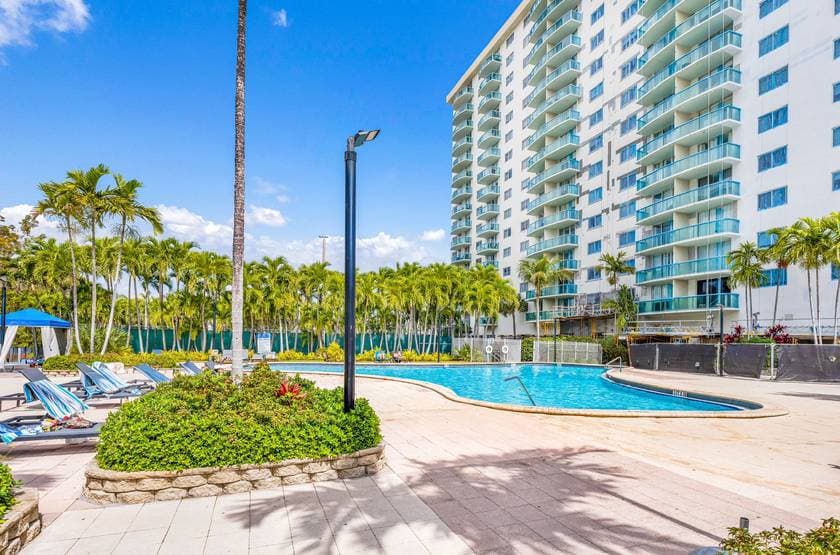 White high-rise with teal balconies beside a palm-lined pool deck